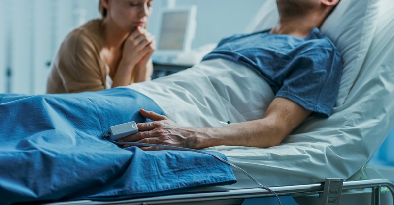 Femeie rugându-se lângă patul de spital pentru soțul ei. Sursă foto depositphotos.com