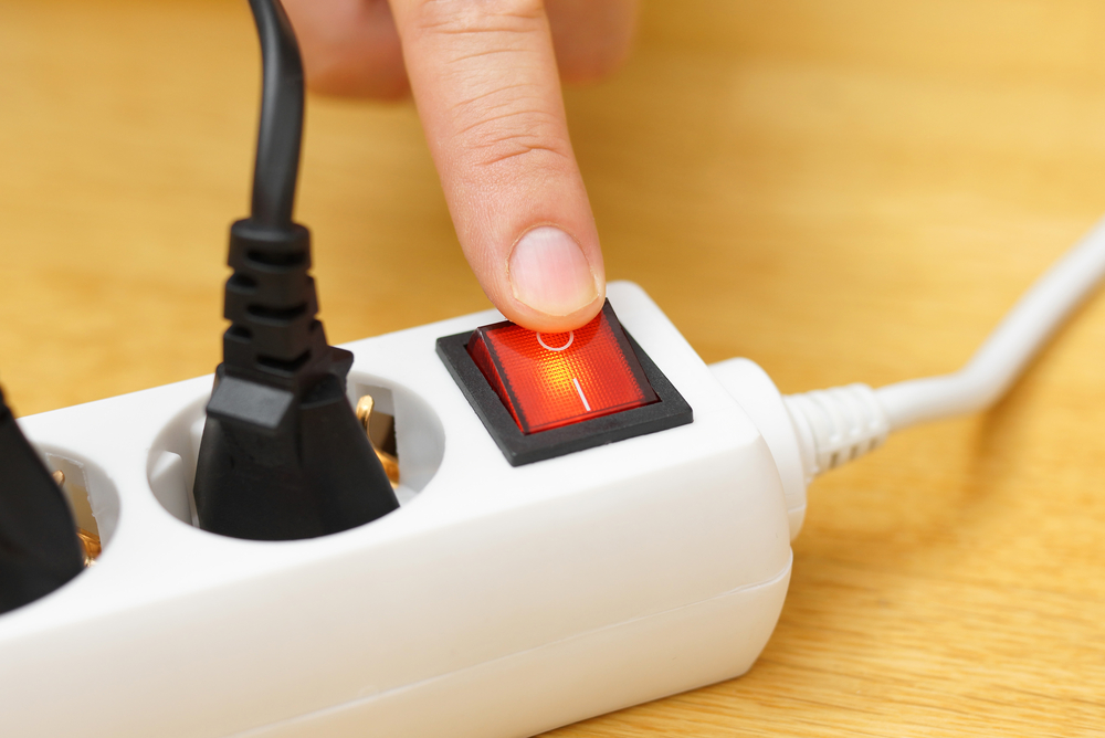 O mână apasă butonul oprire de pe prelungitor pentru a economisi energie electrică / Foto: depositphotos.com